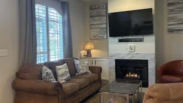 Una sala de estar con sofá, mesa de centro, chimenea, televisor montado en la pared y ventilador de techo.