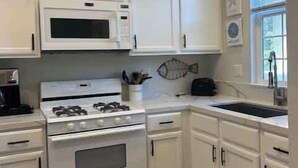 Una cocina con armarios blancos, microondas, estufa y lavaplatos.
