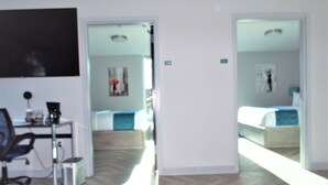 A hotel room with a desk, chair, and a bed. There is a hallway leading to another room. - Cozy 2-bedroom hotel suites just two blocks from Downtown Athens. (Athens)