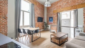 Ein modernes Wohnzimmer mit Backsteinwand, einem Holzesstisch mit Stühlen, einer Couch und einem an der Wand befestigten Fernseher.