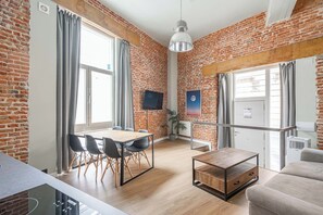 Ein modernes Wohnzimmer mit Backsteinwand, einem Holzesstisch mit Stühlen, einer Couch und einem an der Wand befestigten Fernseher.