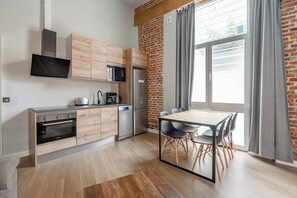 Eine moderne Küche mit Ziegelwand, Holzschränken, einem Edelstahlkühlschrank und einem Essbereich mit Tisch und Stühlen.