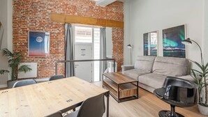 Ein Zimmer mit Backsteinwand, einem Holztisch, einer Couch und zwei Blumentöpfen.