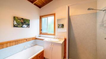 A bathroom with a bathtub, a sink, and a shower. There is a window above the sink and a painting on the wall.