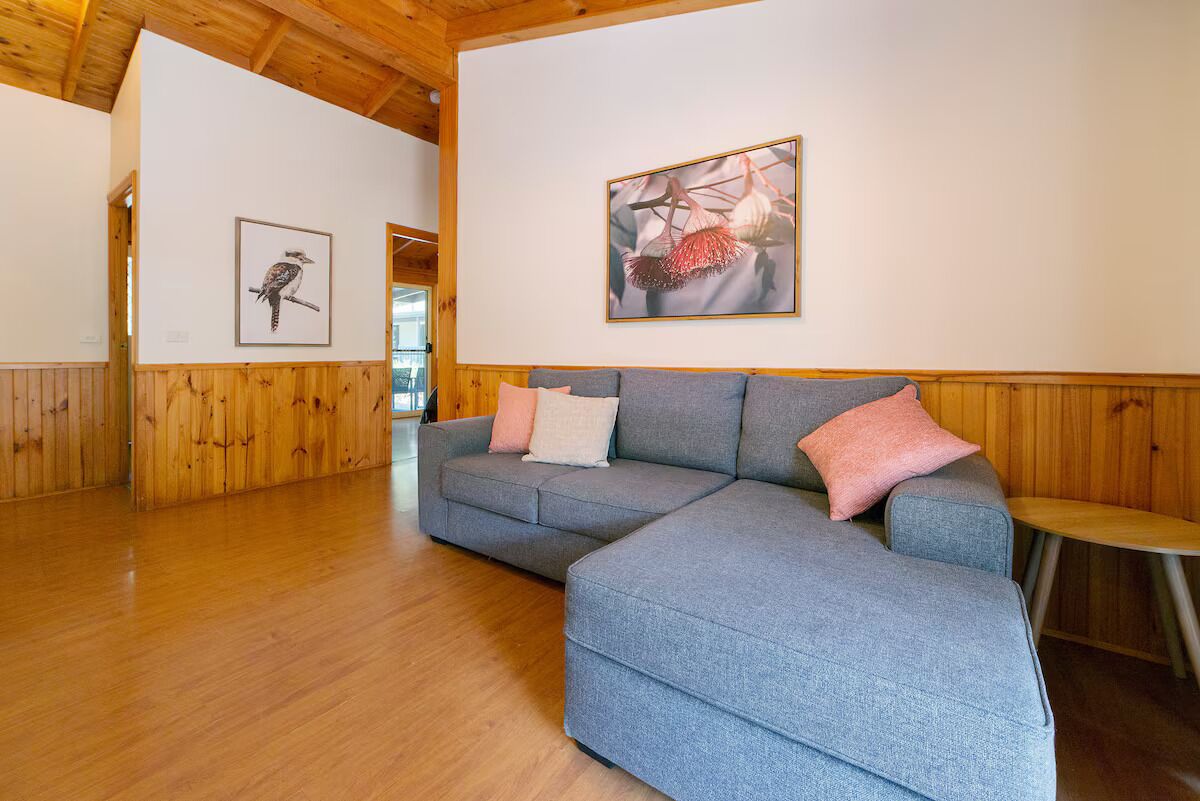 Un salon moderne avec un canapé d’angle gris, des murs recouverts de panneaux en bois et des œuvres d’art encadrées accrochées aux murs.