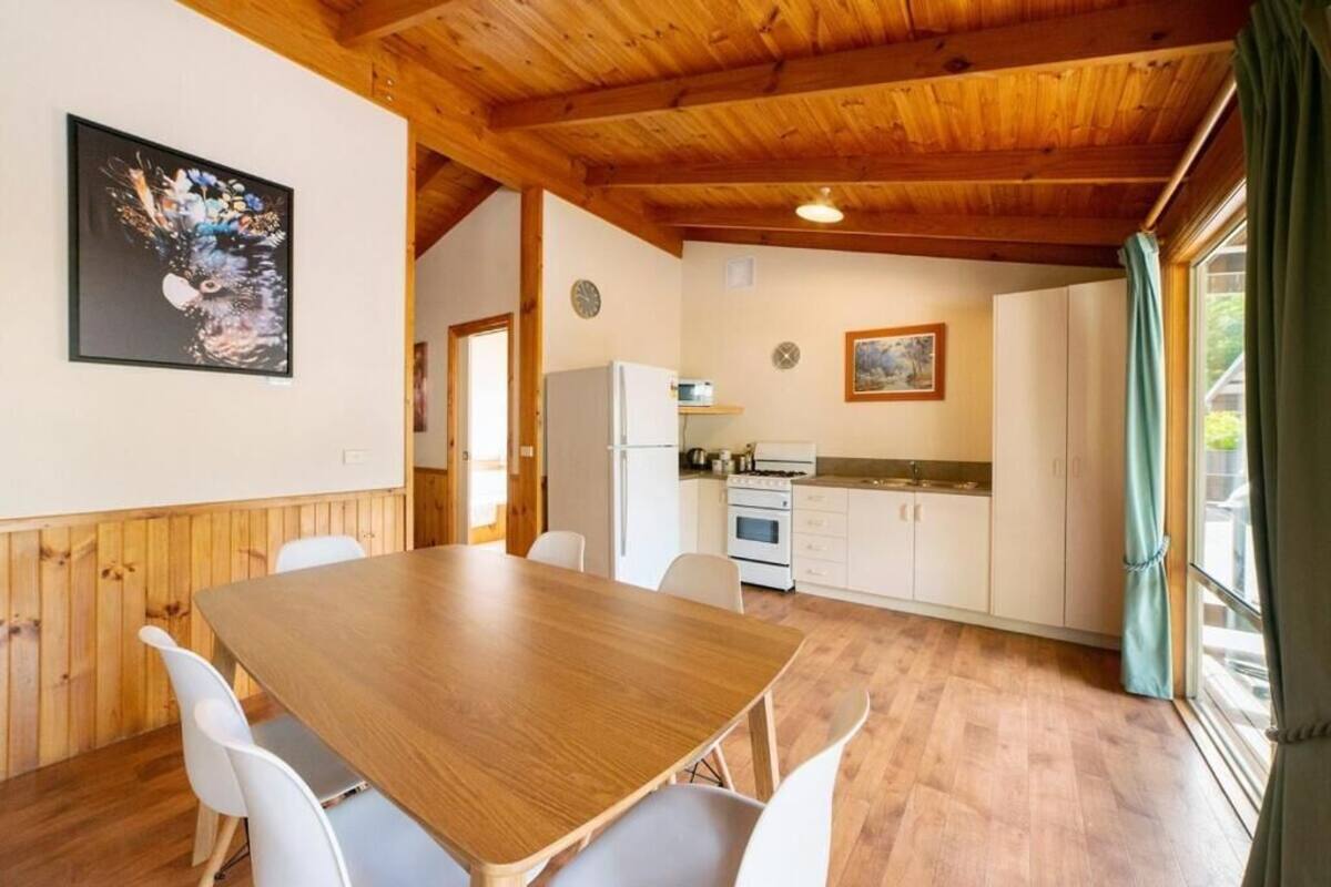 A wooden-paneled room with a dining table and chairs, a kitchen area, and a large window with curtains.