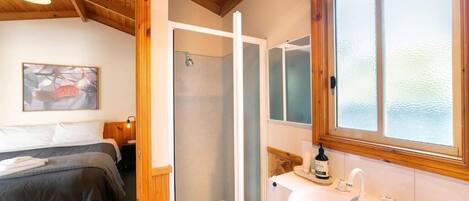 A hotel room with a bed, a shower, a sink, and a window with frosted glass.
