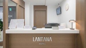 Una reception d'hotel con finiture in legno, uno schermo digitale e un cartello con la scritta 'LANTANA HOTEL'.