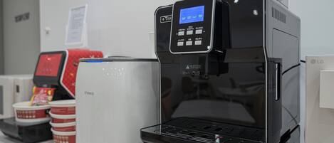 Una máquina de café con pantalla digital, un dispensador de bebidas rojo y tazas apiladas.