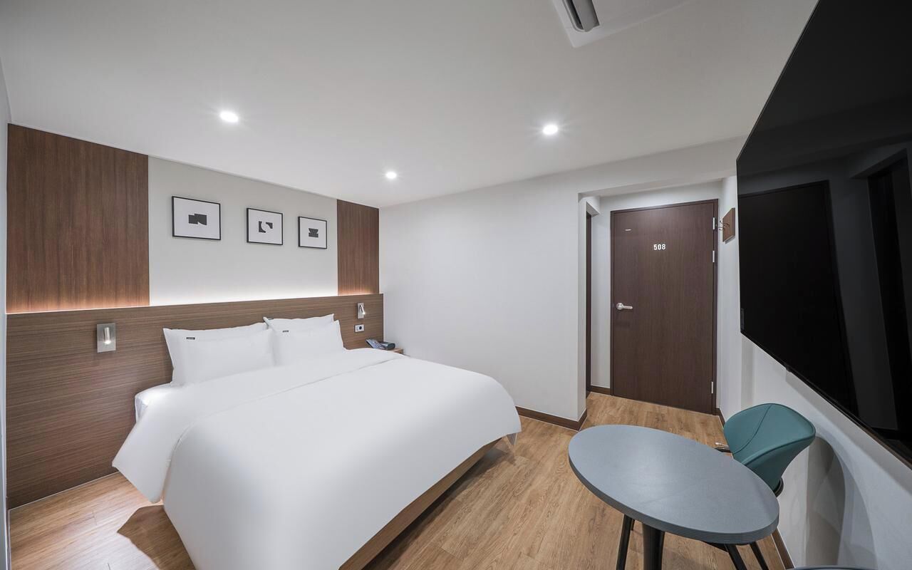 Habitación de hotel con una cama grande, una mesita, un televisor y una puerta con un número.