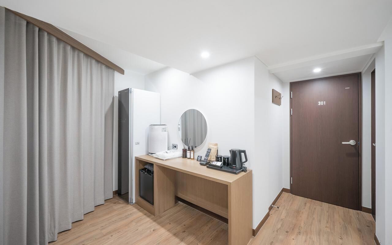 Habitación de hotel con un escritorio de madera, una cafetera, un pequeño cubo de basura y una puerta con el número 301.