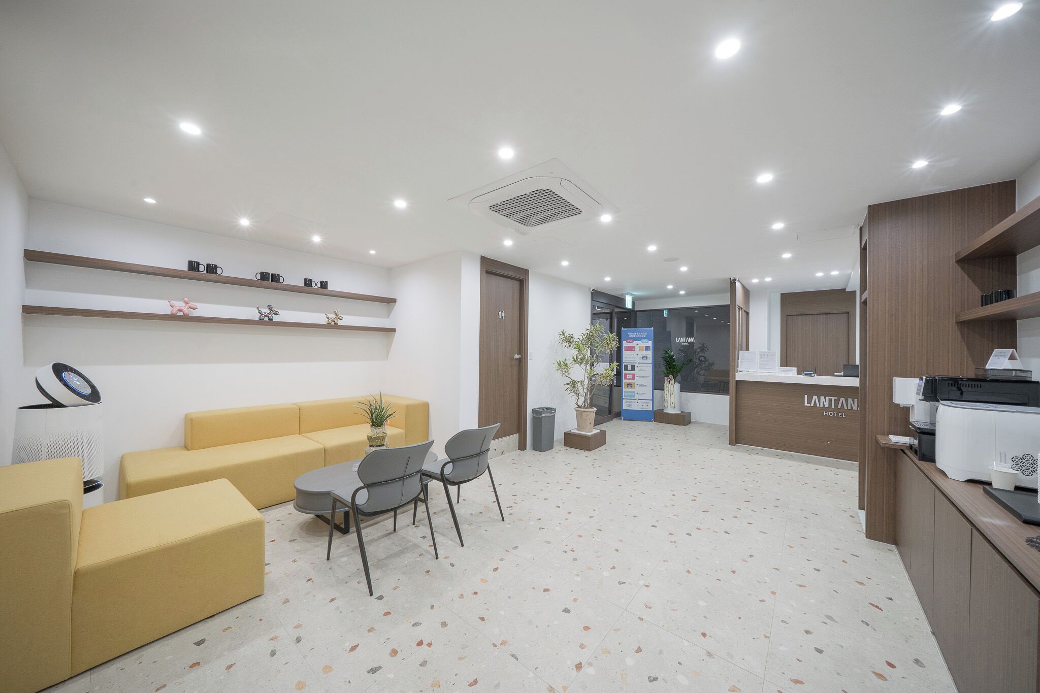 A hotel reception area with a reception desk, seating area with yellow sofas, and a coffee machine.