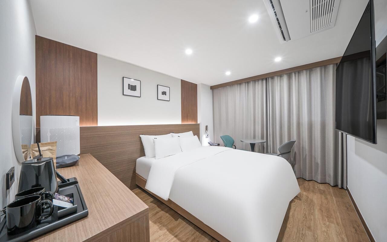 Una habitación de hotel moderna con una cama grande, un escritorio con cafetera, un televisor y una ventana con cortinas.