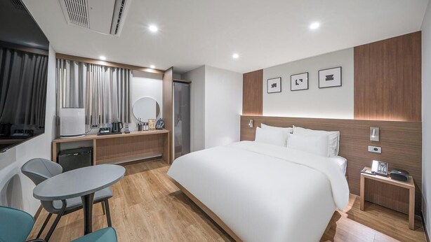 Una camera d'albergo moderna con un letto grande, una scrivania con sedia, un tavolino, uno specchio e un comodino con telefono.
