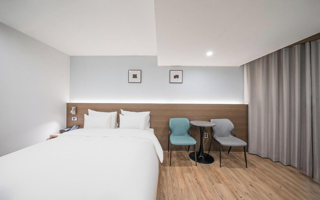 A hotel room with a bed, two chairs, a small table, and a curtain.