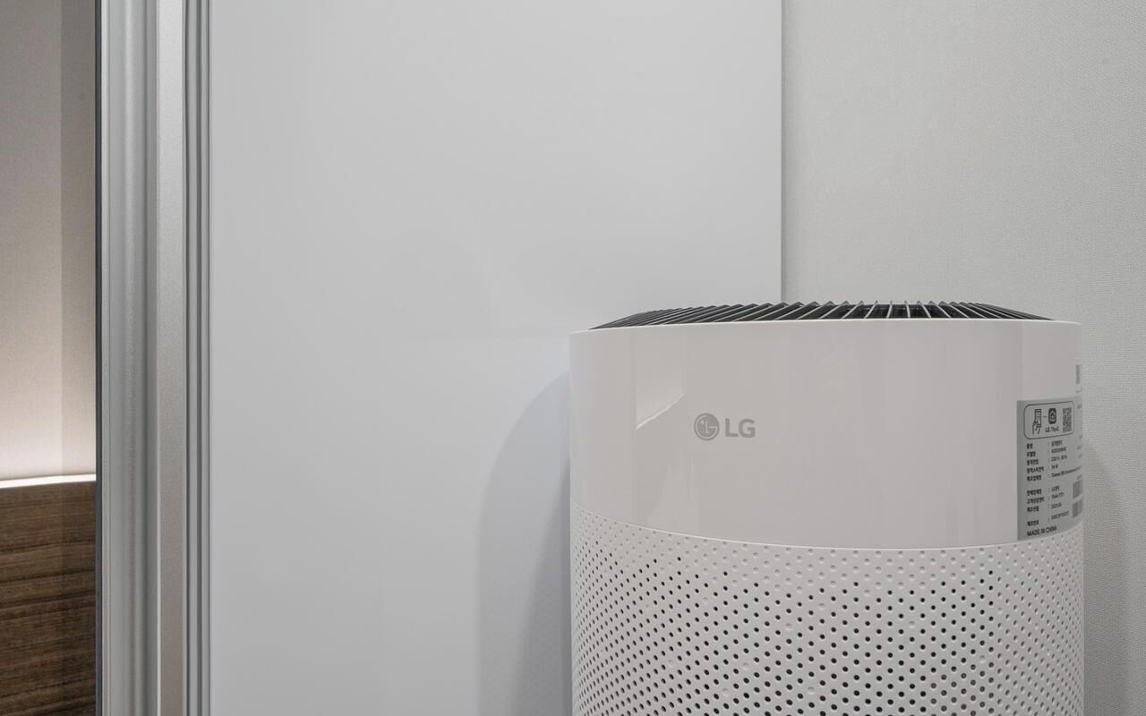 A white LG air purifier in a room with a white wall and a wooden floor.