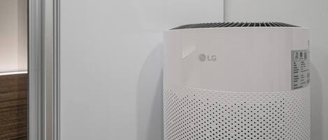A white LG air purifier in a room with a white wall and a wooden floor.
