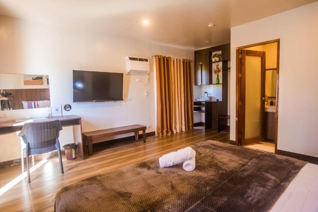 Habitación de hotel con cama, escritorio con silla, televisor y baño visible a través de una puerta abierta.