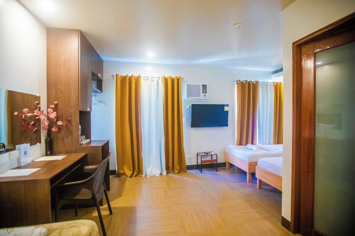 A hotel room with a wooden desk, two beds, a small table, and a TV.