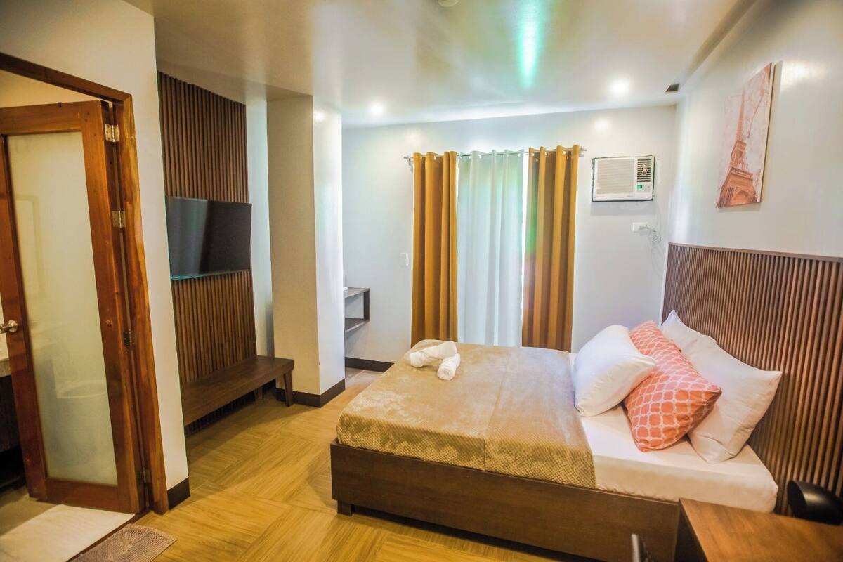 A hotel room with a bed, a TV mounted on the wall, and a window with curtains.
