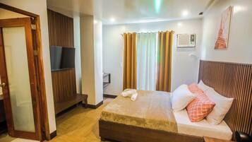 A hotel room with a bed, a TV mounted on the wall, and a window with curtains.