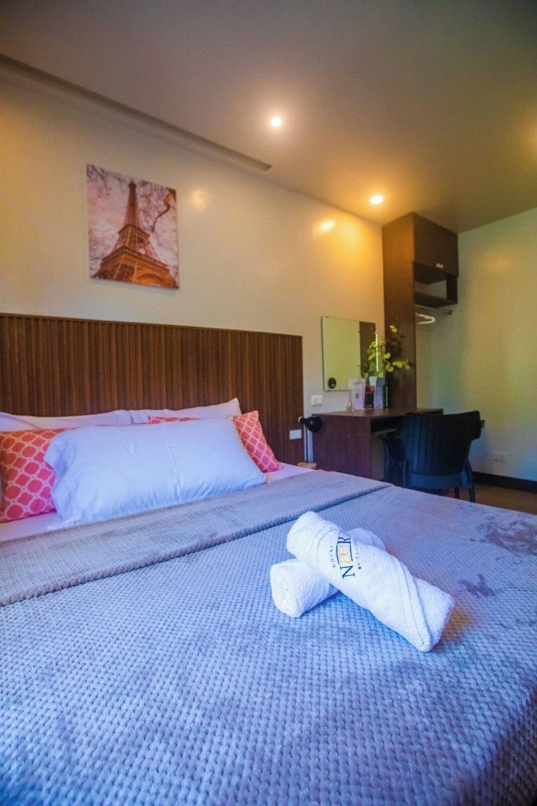 A hotel room with a bed, a desk, a chair, a mirror, and a picture of the Eiffel Tower on the wall.