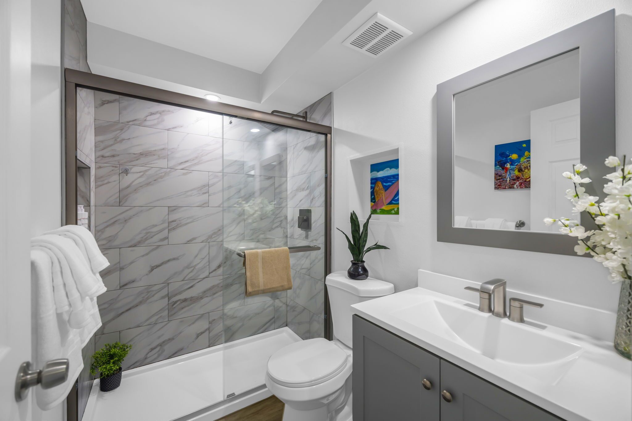 A modern bathroom with a glass-enclosed shower, a toilet, a sink, and a mirror.