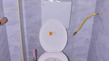 A bathroom with a toilet, a bidet, a toilet brush, and a toilet paper holder.