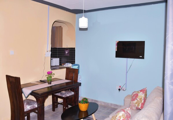 A dining area with a table, chairs, a small potted plant, and a television mounted on the wall.