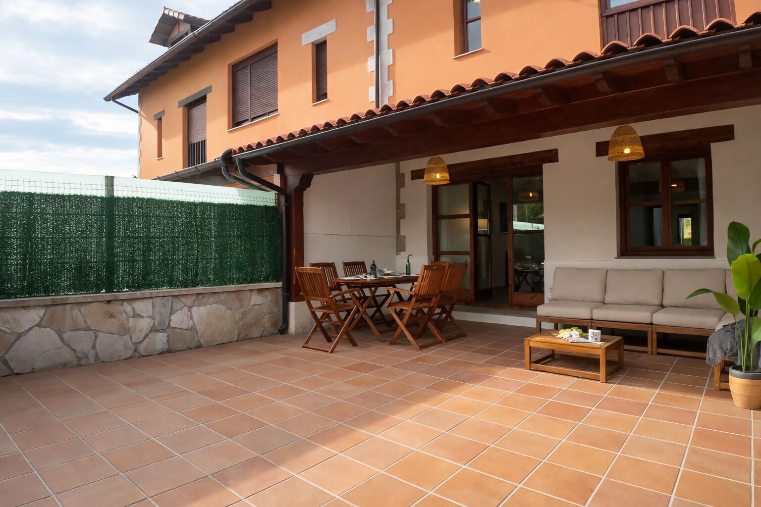 A covered patio with a dining table and chairs, a sofa, and a potted plant.