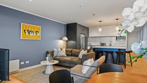 Una sala de estar moderna con un sofá, una mesa de centro y sillas. Incluye una zona de cocina con taburetes de bar y una mesa de comedor.