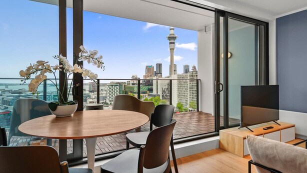 Un apartamento moderno con balcón, una mesa de comedor, sillas, un televisor y una orquídea en maceta.