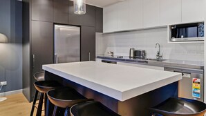 Una cocina moderna con una isla grande, armarios oscuros, electrodomésticos de acero inoxidable y taburetes de bar.