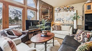 Een gezellige woonkamer met een open haard, een grote televisie en een prachtig uitzicht op de bergen door de ramen.