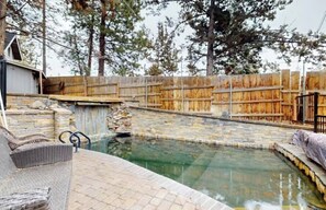A swimming pool with a stone wall and wooden fence, surrounded by trees. - Westside Paradise - Hottub, Home Theater & Pool! (Bend)