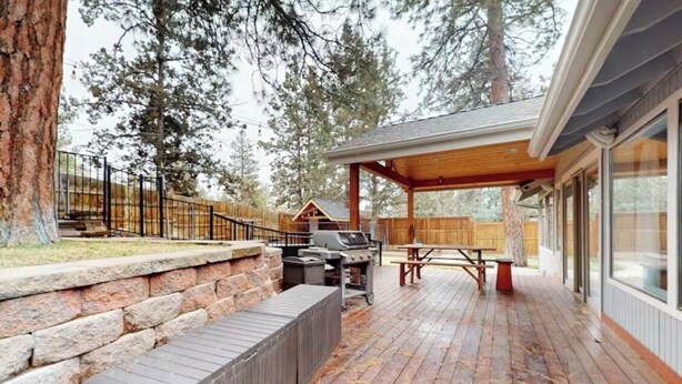 Una terraza techada al aire libre con una parrilla, asientos y vistas a un área boscosa.