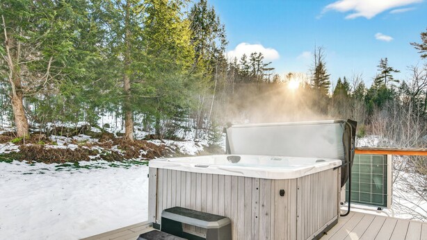 Ein Whirlpool auf einer Holzterrasse mit verschneiter Landschaft und Bäumen im Hintergrund.