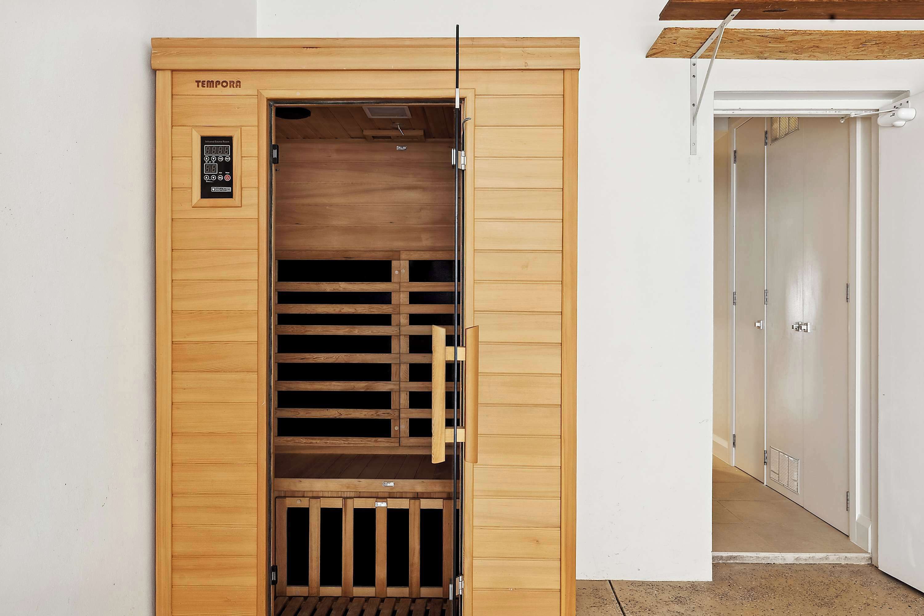 Uma sauna de madeira com painel de controle, portas deslizantes e um banco interno.