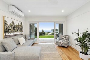A modern living room with a grey sofa, a striped armchair, and a large potted plant. - Panoramic Ocean Views | N. Avoca, Sleeps 10 (North Avoca)