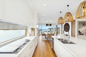A modern kitchen with a view of the ocean, wooden flooring, and pendant lights. - Panoramic Ocean Views | N. Avoca, Sleeps 10 (North Avoca)