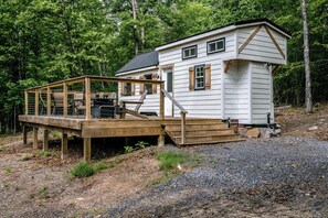 Une cabane dotée d’une terrasse en bois, d’un petit porche et d’une allée gravillonnée.