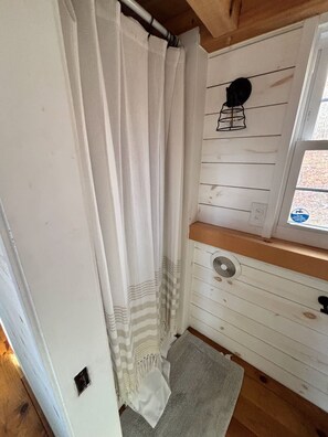 Une salle de bain avec un rideau de douche, une fenêtre donnant sur un beau paysage et une étagère en bois.