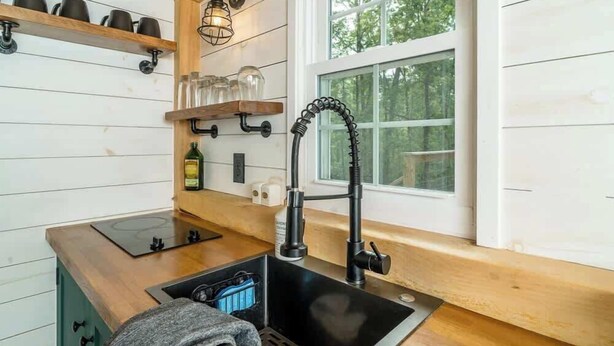A kitchen with a black sink, wooden shelves, and a window with a view of trees. - Amazing TinyHome on private 48Acres in Massanutten (McGaheysville)