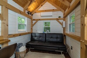 Interior acogedor de una cabaña con un sofá de cuero, vigas de madera y ventanas amplias.