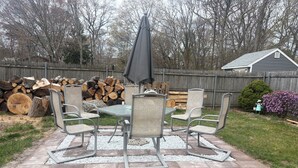 En terrasse med et bord og stole, omgivet af et træhegn og træer.