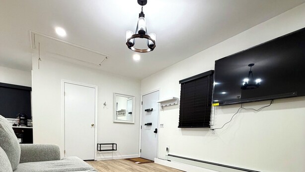 En moderne stue med sofaarrangement, et fladskærms-tv på væggen og en loftlampe.