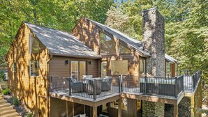 Una baita di legno a due piani con un camino in pietra, un patio con posti a sedere all'aperto e una scala che conduce all'ingresso.