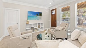 Una sala de estar con un sofá color beige, una mesa de centro de vidrio y un televisor montado en la pared.