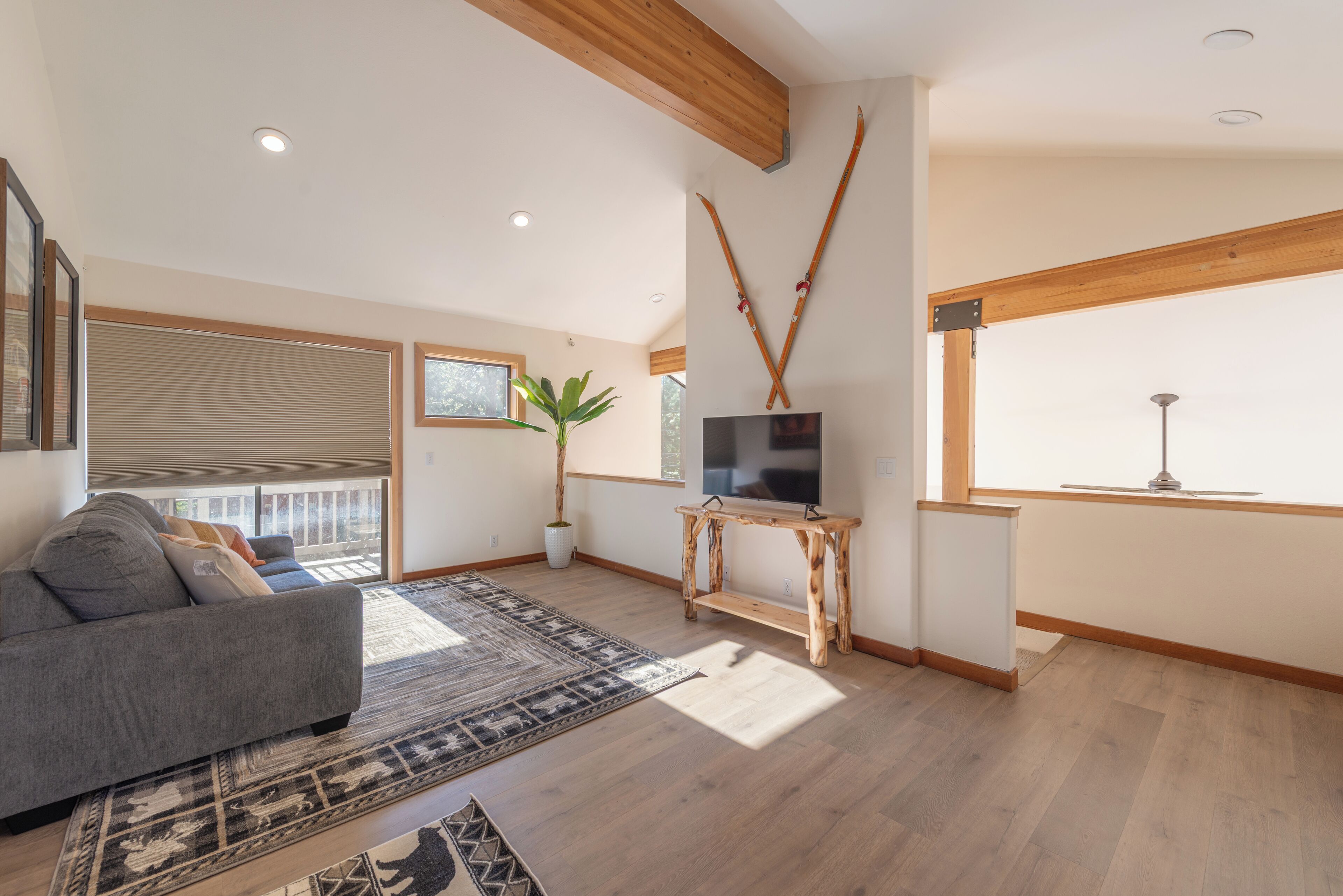 Una sala de estar con un sofá gris, un mueble de televisión de madera y un ventanal con persianas.