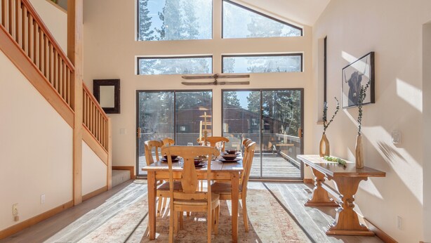 Un comedor espacioso con techo alto y ventanas grandes, muebles de madera y una escalera.